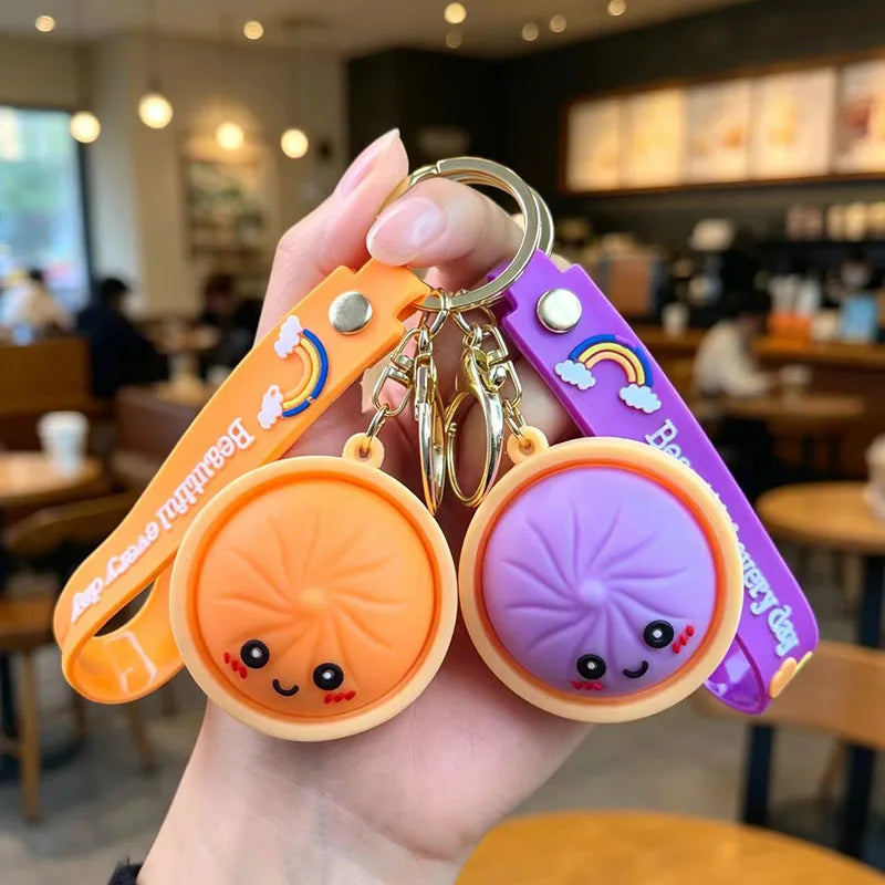 A hand holds several cute bao bun silicone keychains in orange and purple colors.