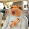 A plush capybara car neck pillow with a small orange accent sits on a light-colored car seat.
