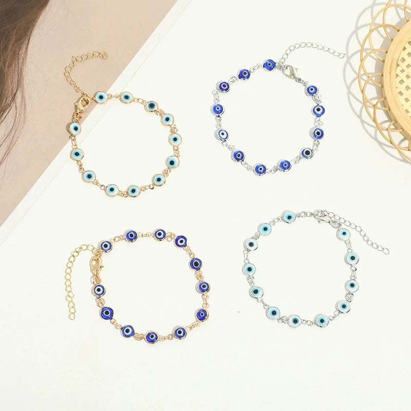 Three gold-plated evil eye charm bracelets with blue and white stones displayed on a white background.