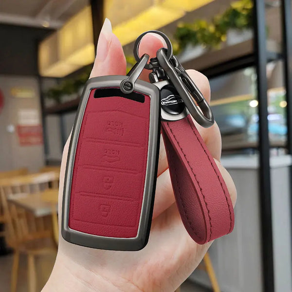 A hand holds a maroon zinc alloy car key case with a leather strap and metal clip.