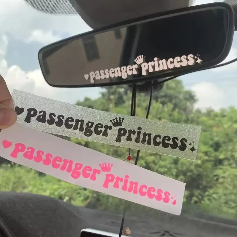 Three pink and green stickers with the text Passenger Princess on a rearview mirror