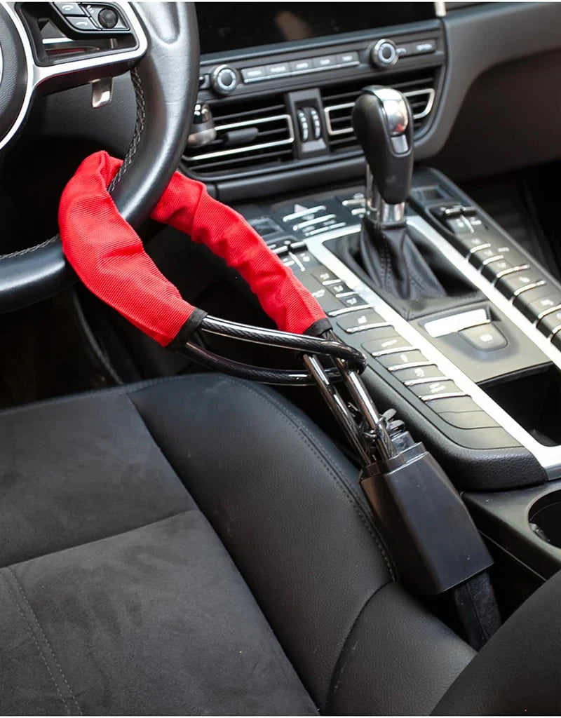 A close-up view of a car steering wheel with a red anti-theft lock attached to the seatbelt strap.