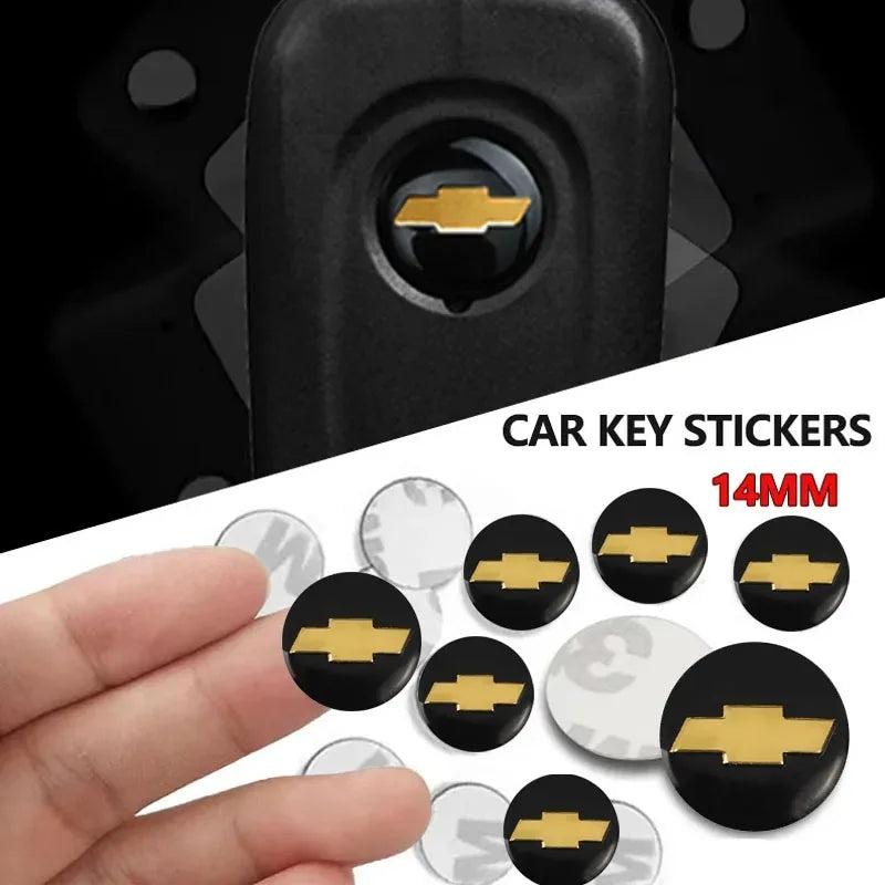 A hand holds a set of 14mm aluminum Chevrolet key emblem stickers for car keys.
