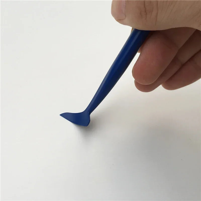 A hand holds a blue vinyl wrap tool with a paddle shape for window tinting and paint protection.