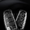 A close-up view of a premium carbon fiber car key case cover resting on a dark, reflective surface.