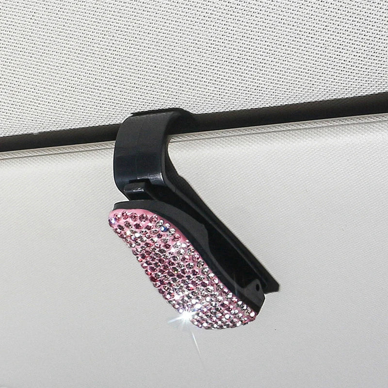 Schwarzer Halter für Sonnenbrillen mit pinkem Kristallakzent, montiert auf einer hellen Oberfläche.