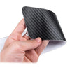A hand holds a black carbon fiber door sill protector with a custom logo.