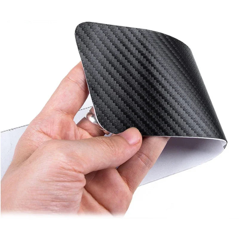 A hand holds a black carbon fiber door sill protector with a custom logo.