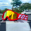 Red off-road motorcycle goggles with yellow mirrored lenses resting on a white surface.