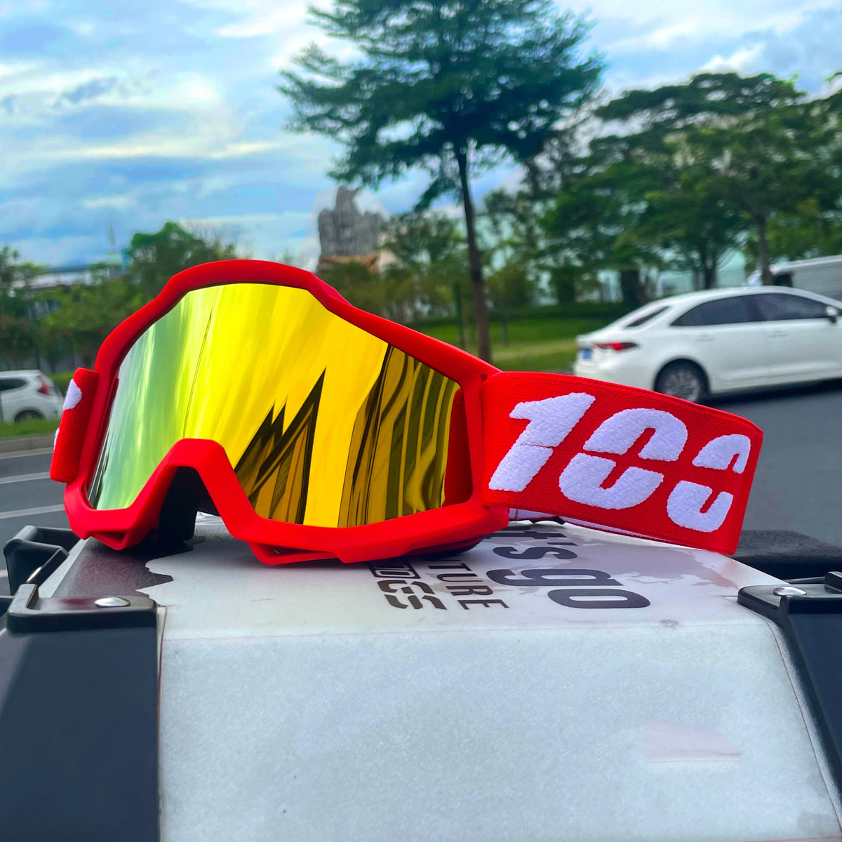 Red off-road motorcycle goggles with yellow mirrored lenses resting on a white surface.