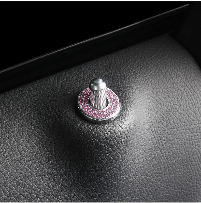 A silver door lock pin trim set with a pink gemstone accent resting on a dark leather surface.