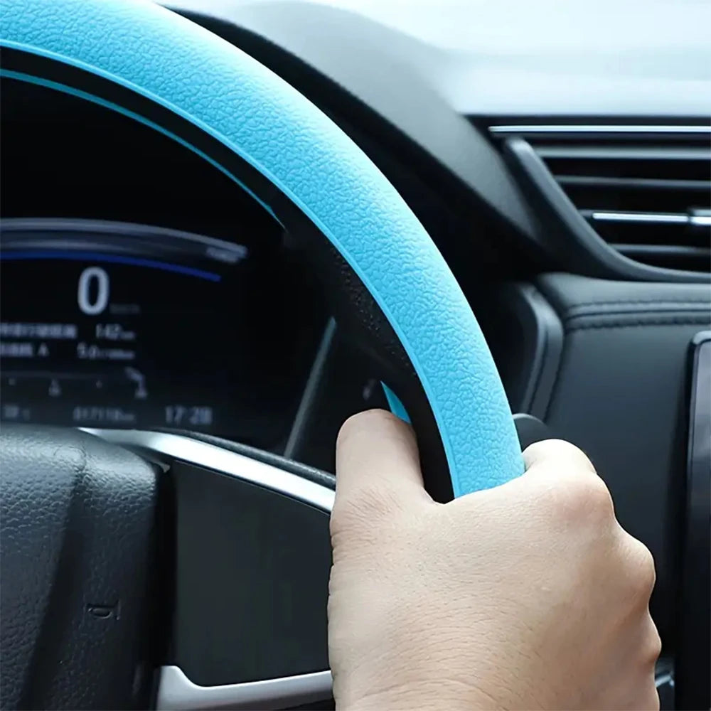 Eine Hand hält eine hellblaue Silikon-Schutzabdeckung für das Lenkrad auf einem schwarzen Auto-Lenkrad.