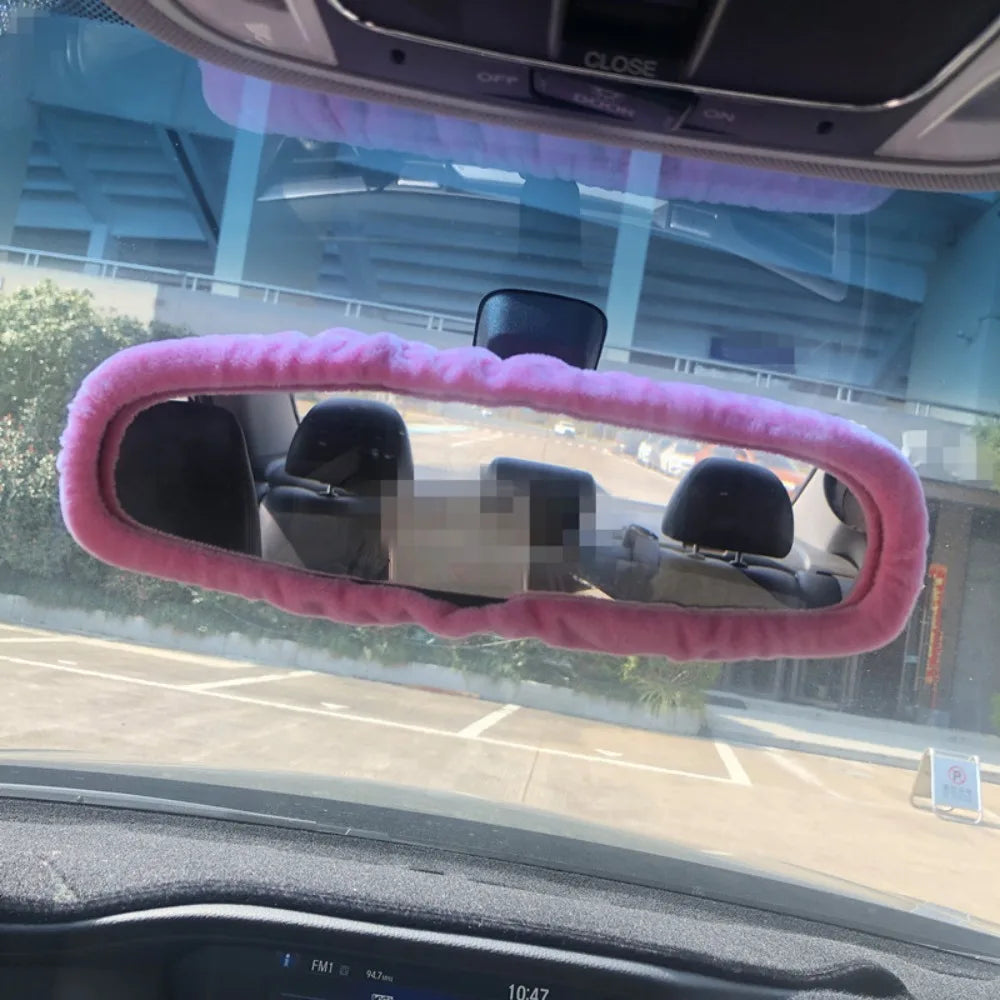 A pink plush cover is placed over the interior of a car's rearview mirror.