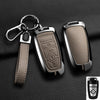A black aluminum alloy key fob cover with a leather strap and keyring displayed on a dark surface.
