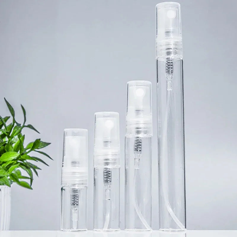 A set of clear glass perfume bottles with silver sprayers standing upright on a white surface.