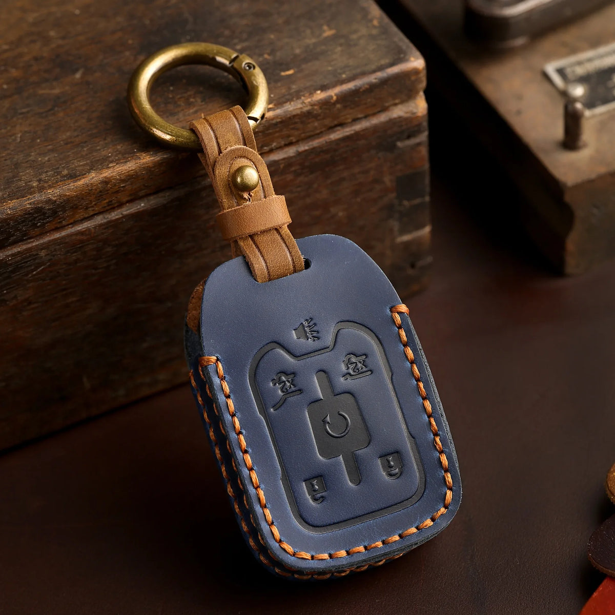 A dark blue leather key cover with a brass ring attached, resting on a wooden box.