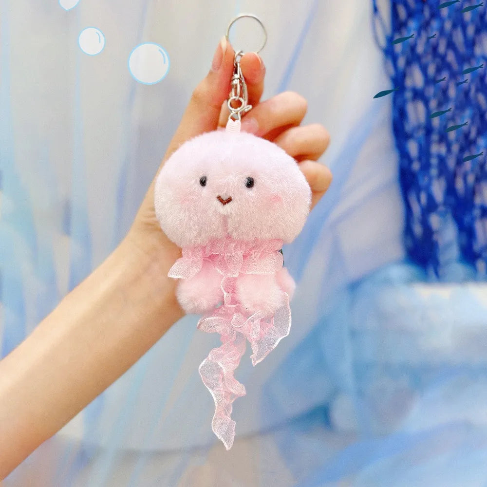 A hand holds a pink plush bunny keychain with soft fur and a gold ring against a light blue background.