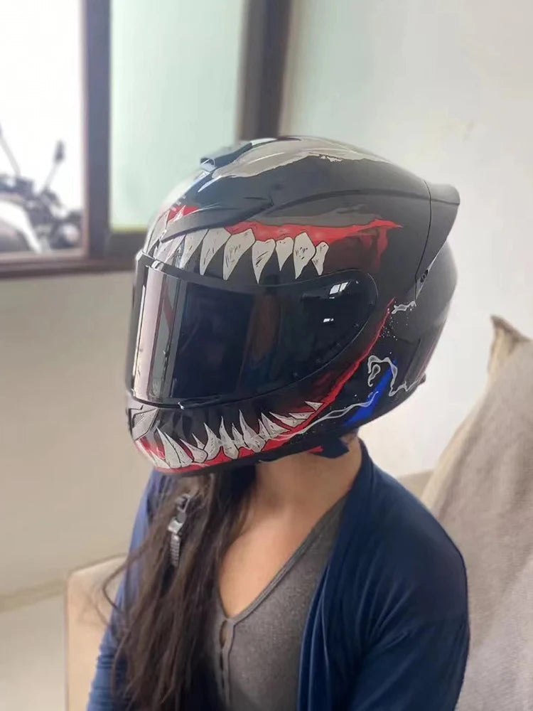 A black full face motorcycle helmet with a fierce, toothy graphic design is shown on a person's head.