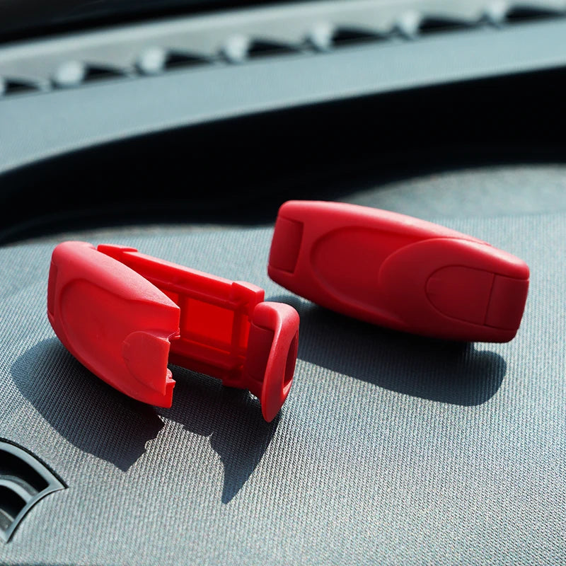 A close-up of a red comfort-adjustable seat belt clip resting on a gray automotive surface.
