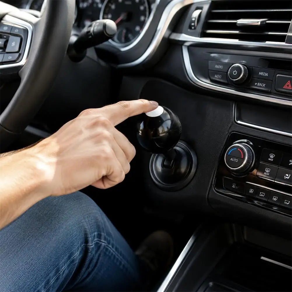 A hand presses a black start button joystick on a car's interior control panel.