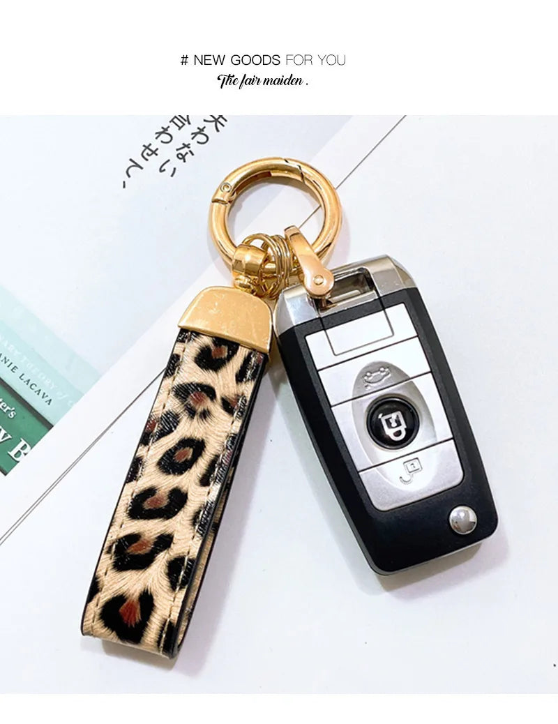 Llavero con anillo dorado y diseño negro y plateado, sujetado por una correa de cuero estampado de leopardo.