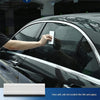 A hand applies a window tinting tool to the glass of a black car.