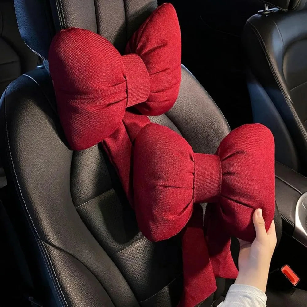 A red bow knot car neck pillow is shown resting on a black leather car seat.