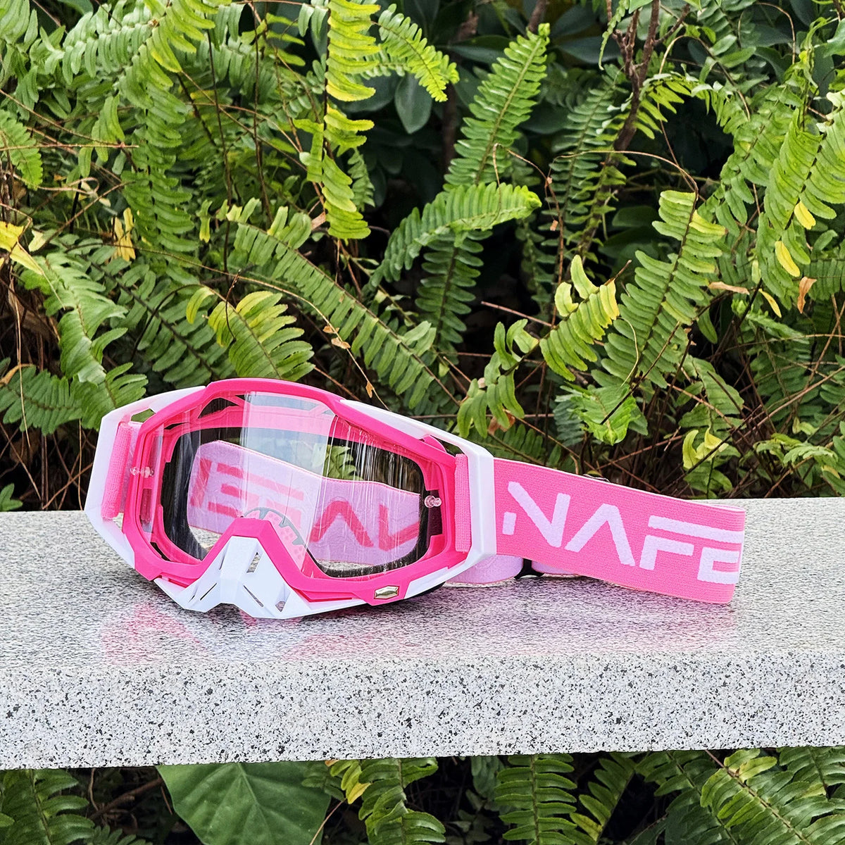 Lunettes de sport pour moto roses et blanches, durables, posées sur une surface grise entourées de feuillage vert.