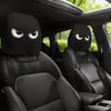 A pair of black car headrest covers with angry eyes are shown inside a vehicle cabin.