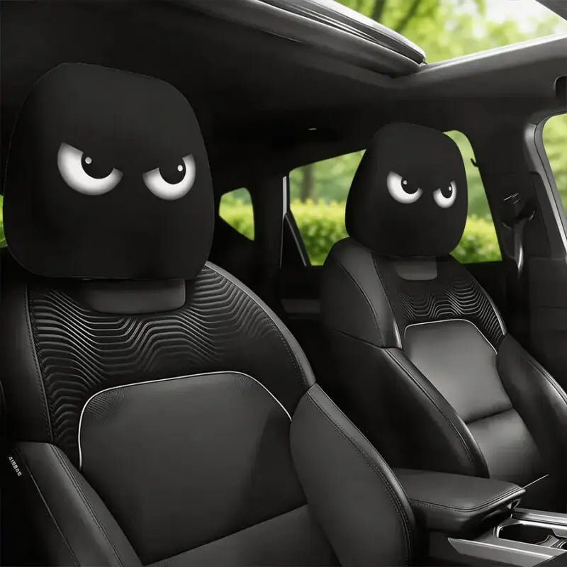 A pair of black car headrest covers with angry eyes are shown inside a vehicle cabin.