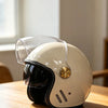 A cream-colored retro motorcycle helmet with a clear visor resting on a wooden surface.