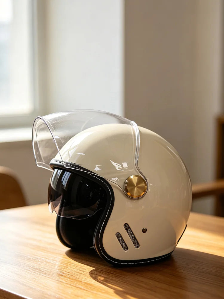 A cream-colored retro motorcycle helmet with a clear visor resting on a wooden surface.