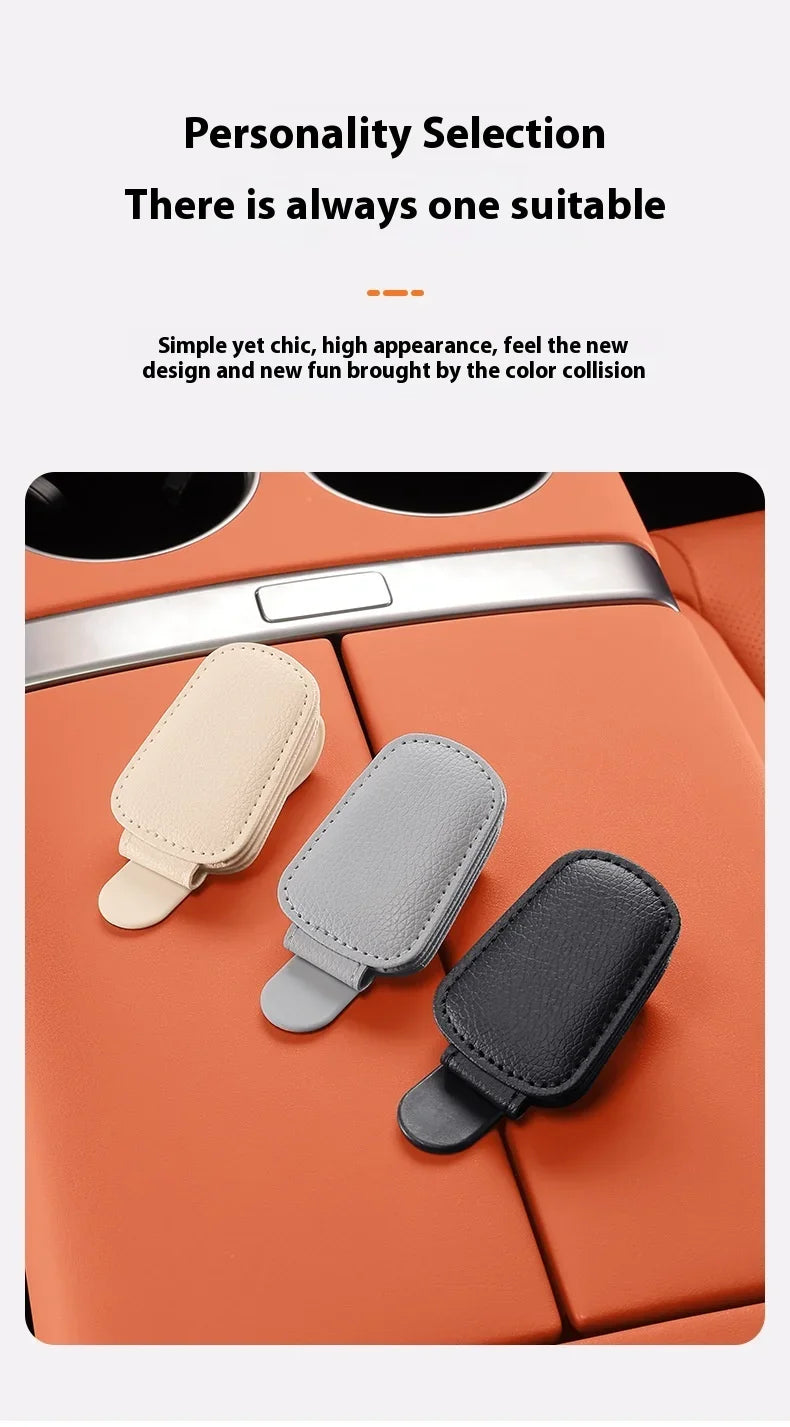 Three magnetic leather sunglasses holders in beige, gray, and black resting on an orange car sun visor.