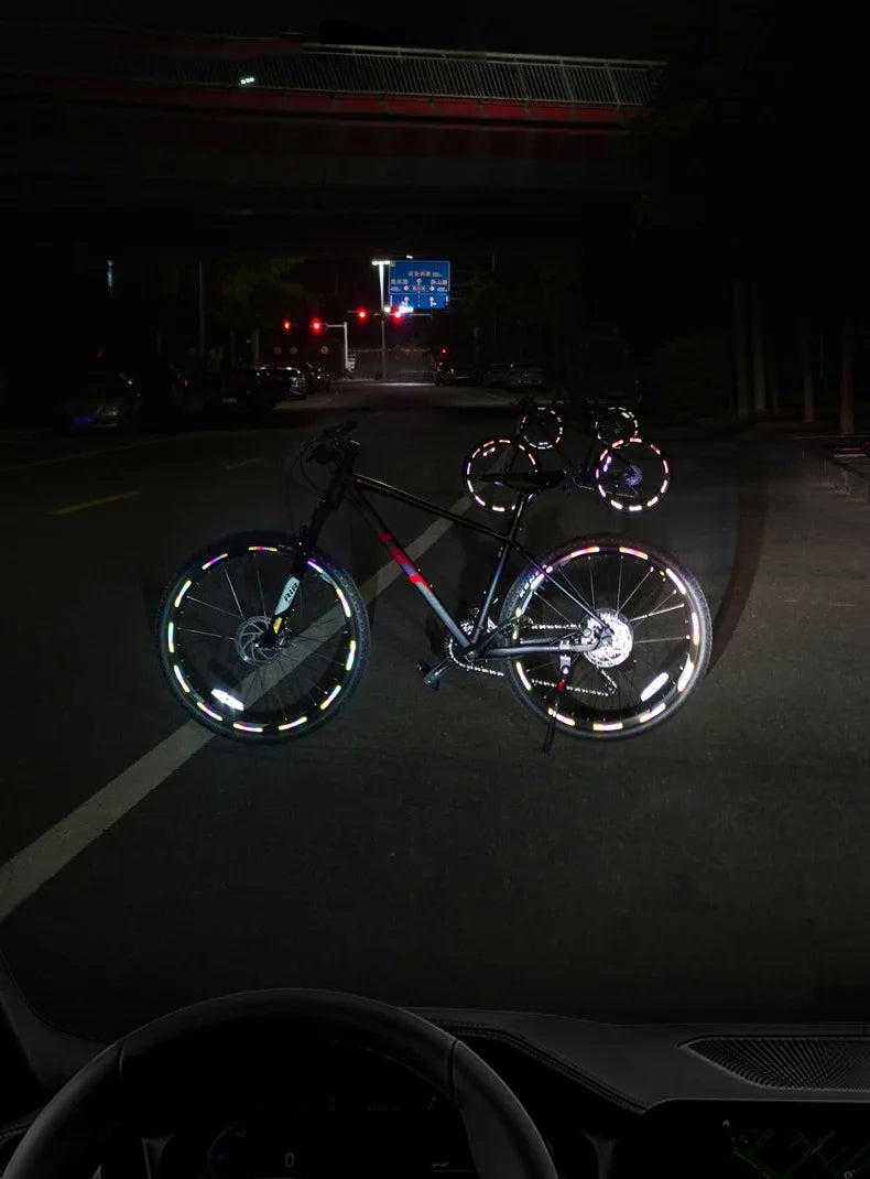 A bicycle with reflective safety stickers on the wheels is parked on a dark road at night.