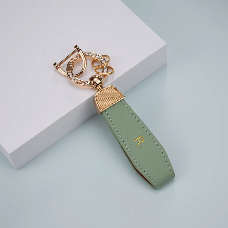 A gold-toned TPU car key fob cover with a leather strap and a key ring is displayed on a white surface.