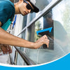 A person uses a professional window tinting tool to apply a film to a glass pane.