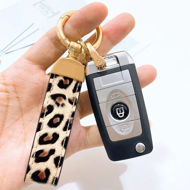 Primer plano de un llavero dorado con correa de cuero estampado de leopardo unido a un dispositivo electrónico negro.