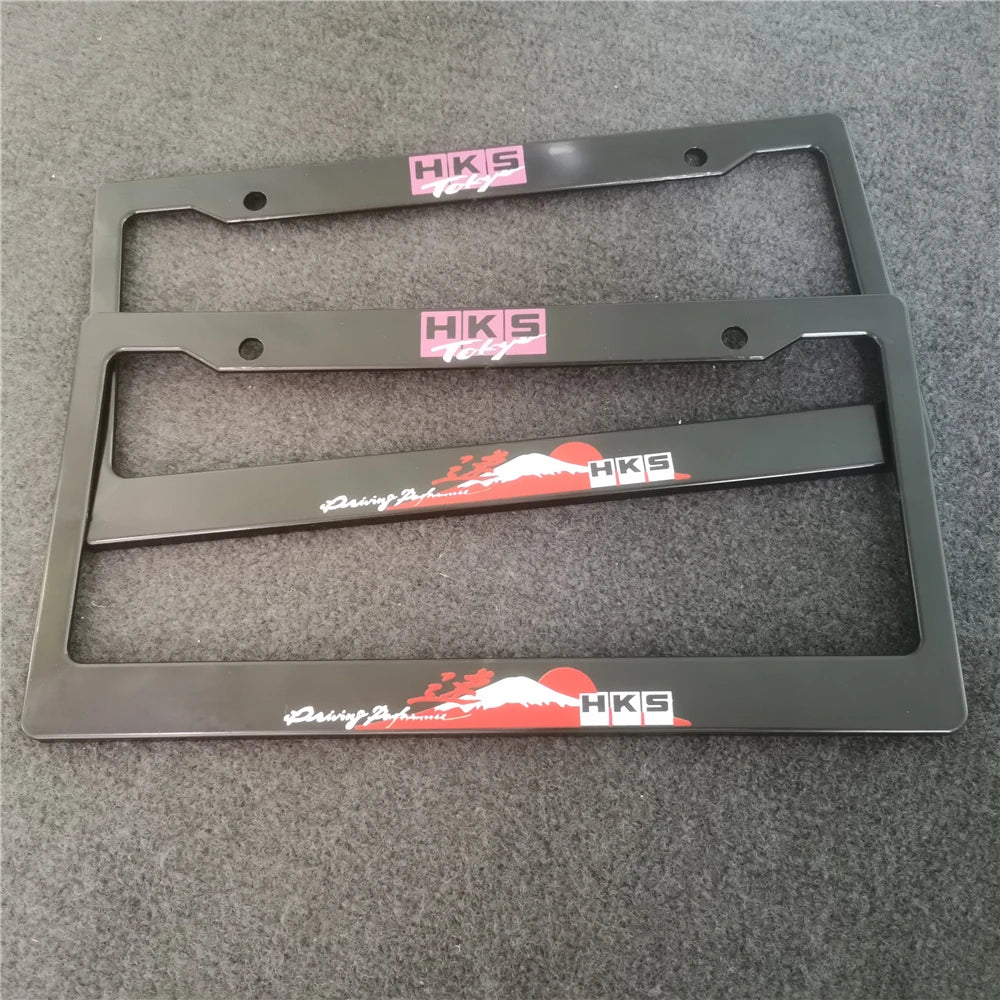 A black license plate frame decoration with HKS branding and a racing theme, shown against a gray background.