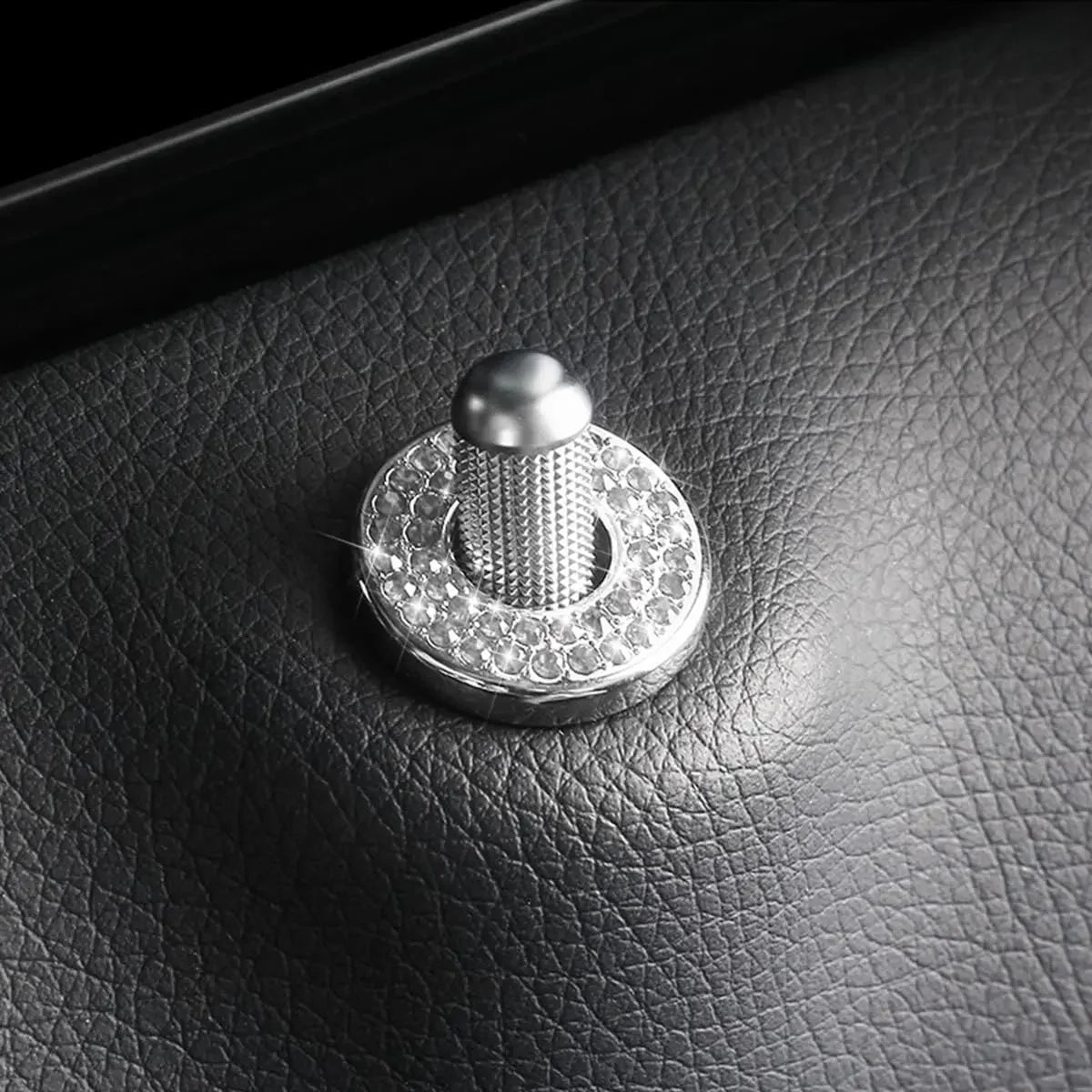 Close-up of a sparkly rhinestone car door lock decoration resting on a dark leather surface.