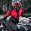 A person wearing a black and red waterproof motorcycle raincoat is sitting on a silver motorcycle outdoors.