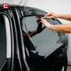 Une main applique ou ajuste un film de teinte de qualité sur la vitre d'une voiture sombre.