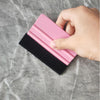 A hand holds a pink felt squeegee tool with a black rubber strip on a gray marble surface.