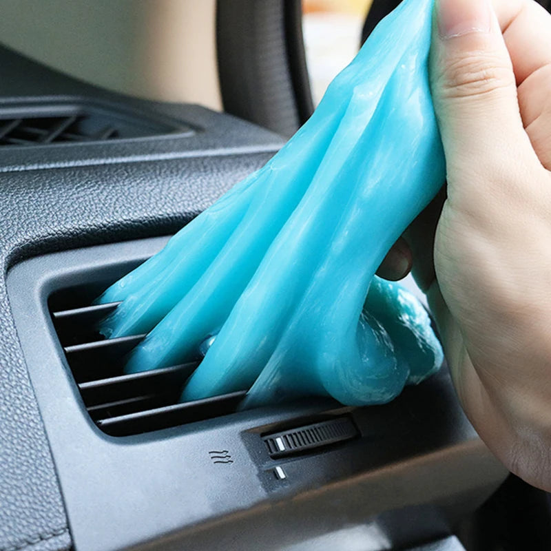 A hand is squeezing a translucent blue gel cleaner for household and car surfaces into a vent or air intake.