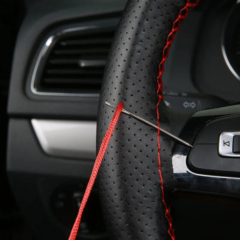 A close-up of a black faux leather steering wheel cover being sewn with red thread and a needle.