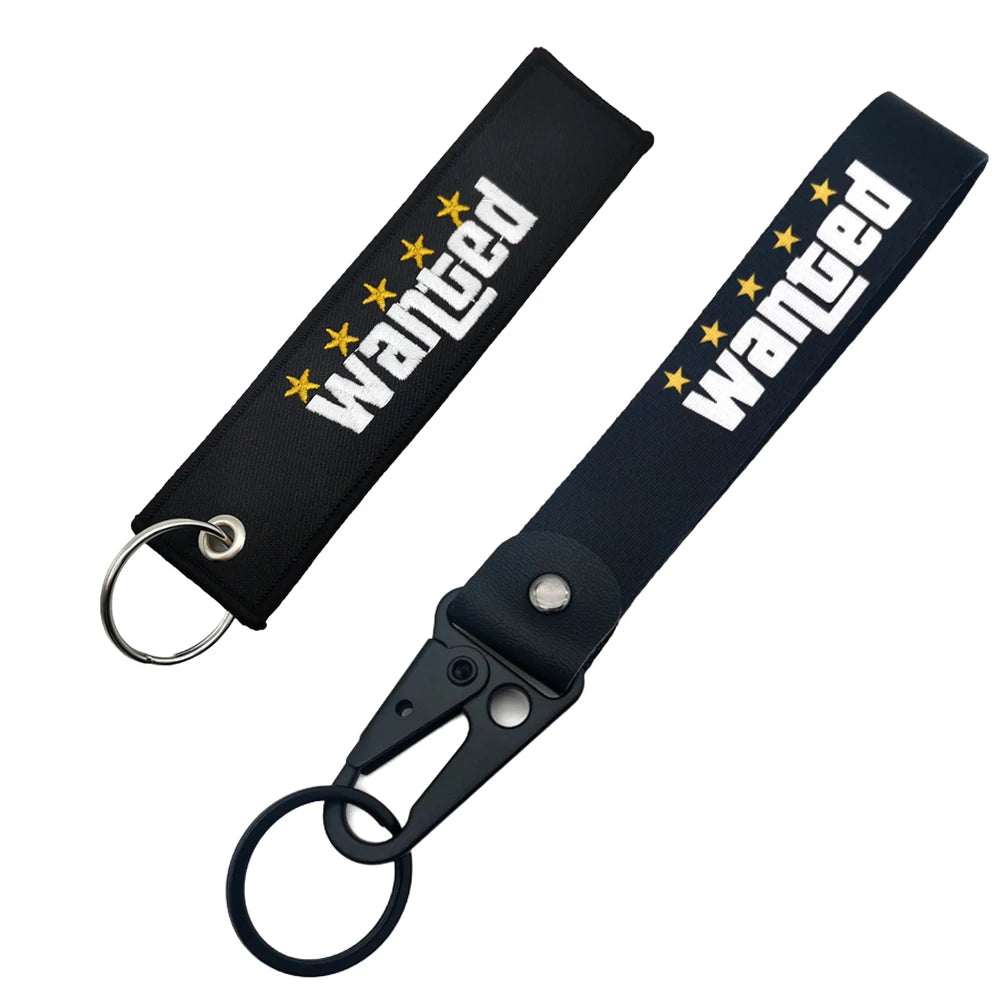 Porte-clés nylon noir avec texte 'wanted' brodé et fermoir métallique.