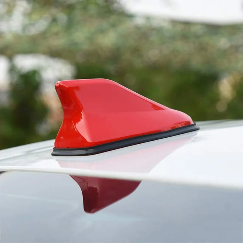 A red shark fin universal car antenna amplifier mounted on a silver car roof.