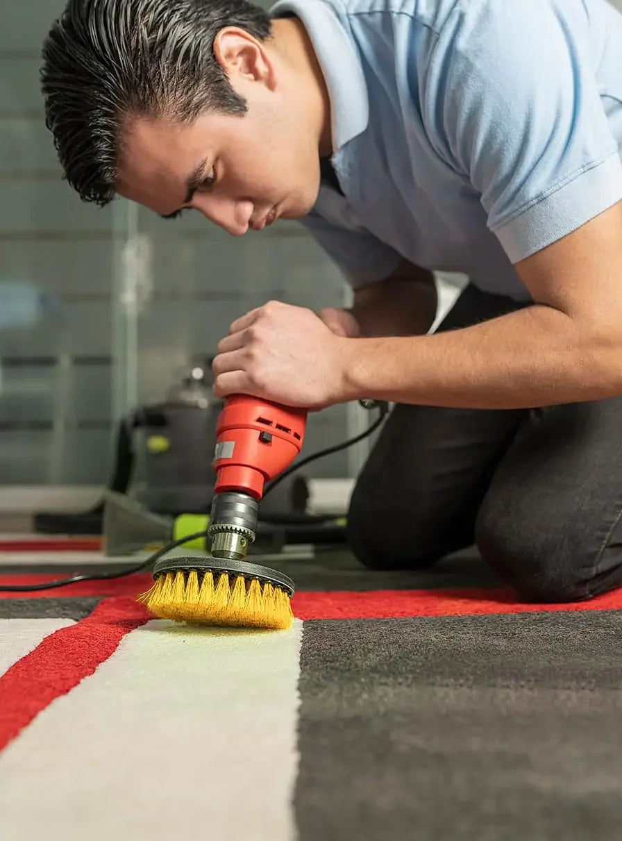 A man is using an orange cleaning brush on a rug to clean the floor.