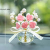 A crystal rose dashboard ornament featuring pink and white roses and pearl accents tied with a white ribbon.