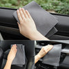A hand is holding a gray coral fleece drying towel against a dark car interior surface.