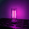 A clear glass cylindrical LED night light with bright pink illumination resting on a black grid surface.